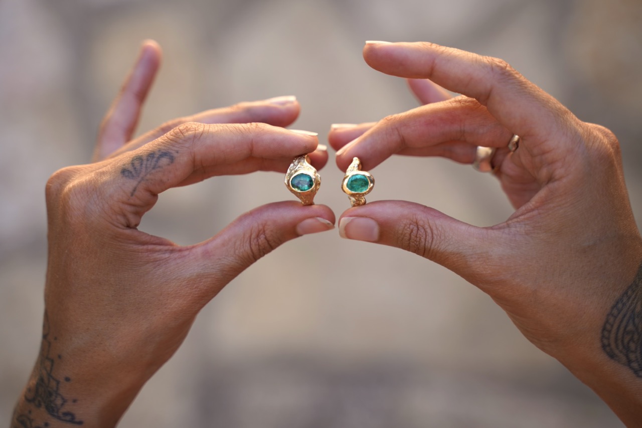 Two hands holding gold rings with emeralds